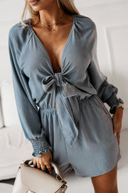 Cloudy Blue tie-front blouson sleeve playsuit with smocked cuffs and a deep V-neckline.