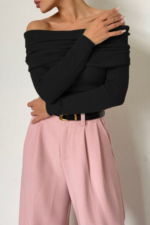 Black off-the-shoulder ribbed drape top with long sleeves, styled with pink trousers.