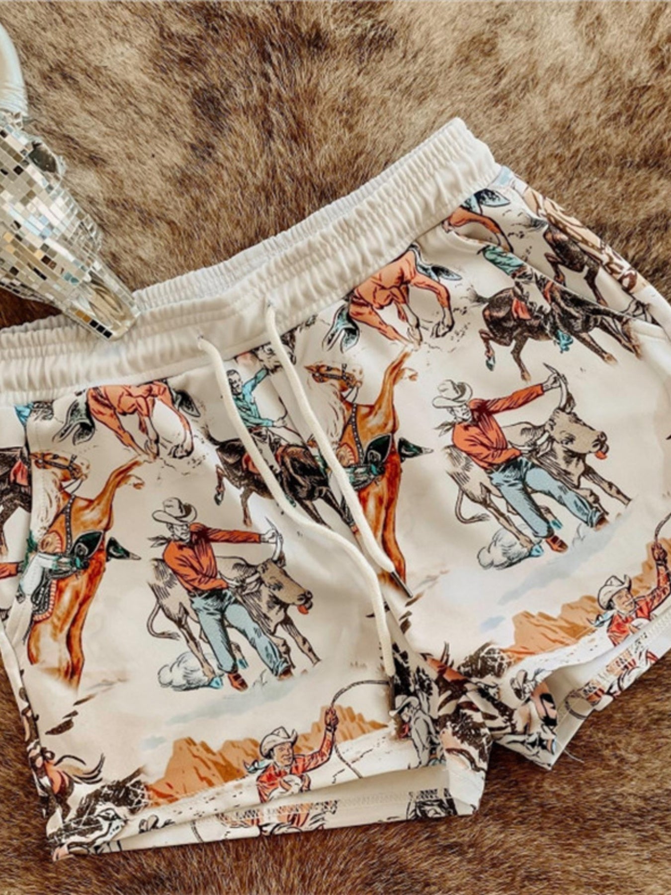White drawstring shorts with a vintage rodeo print and elastic waistband.