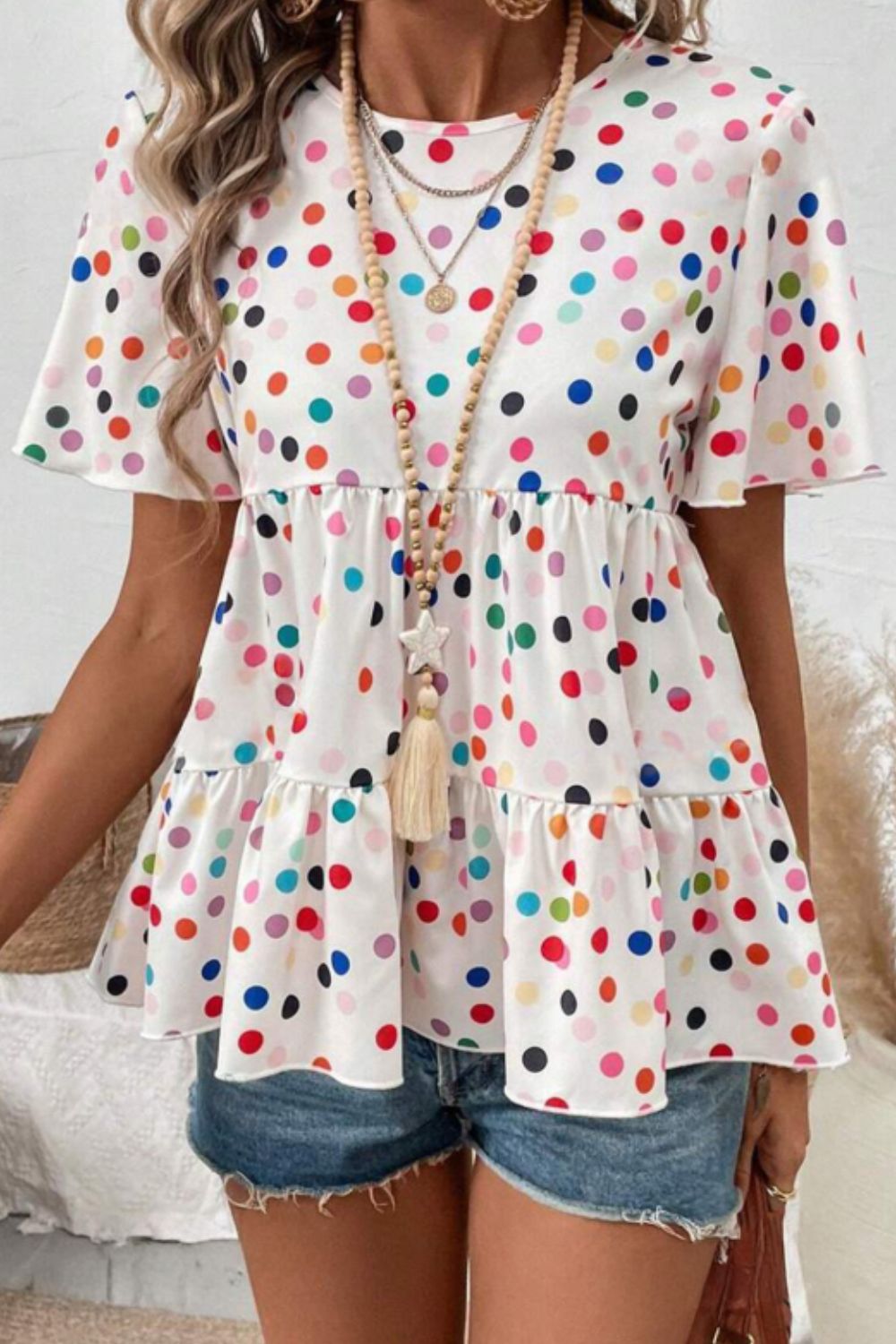 White polka dot tiered babydoll blouse with flutter sleeves and round neck.