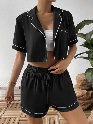 Black cropped pajama set with white contrast trim, featuring a button-up shirt and drawstring shorts.