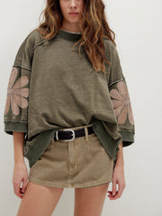 Mineral wash green cotton sweatshirt with pink flower patches on sleeves and raw hem detail.