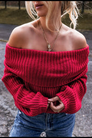 Off-the-shoulder red acrylic sweater with ribbed texture and long sleeves, styled with necklaces.
