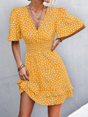 Mustard yellow mini dress with white speckle print, flutter sleeves, smocked waist, and ruffled hem.