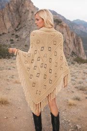 Tan knit poncho with geometric pattern and fringe, styled with black boots.