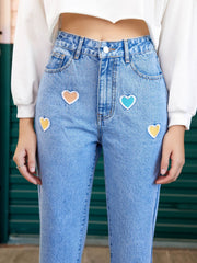 Light wash denim jeans with colorful heart patches and a straight leg cut.