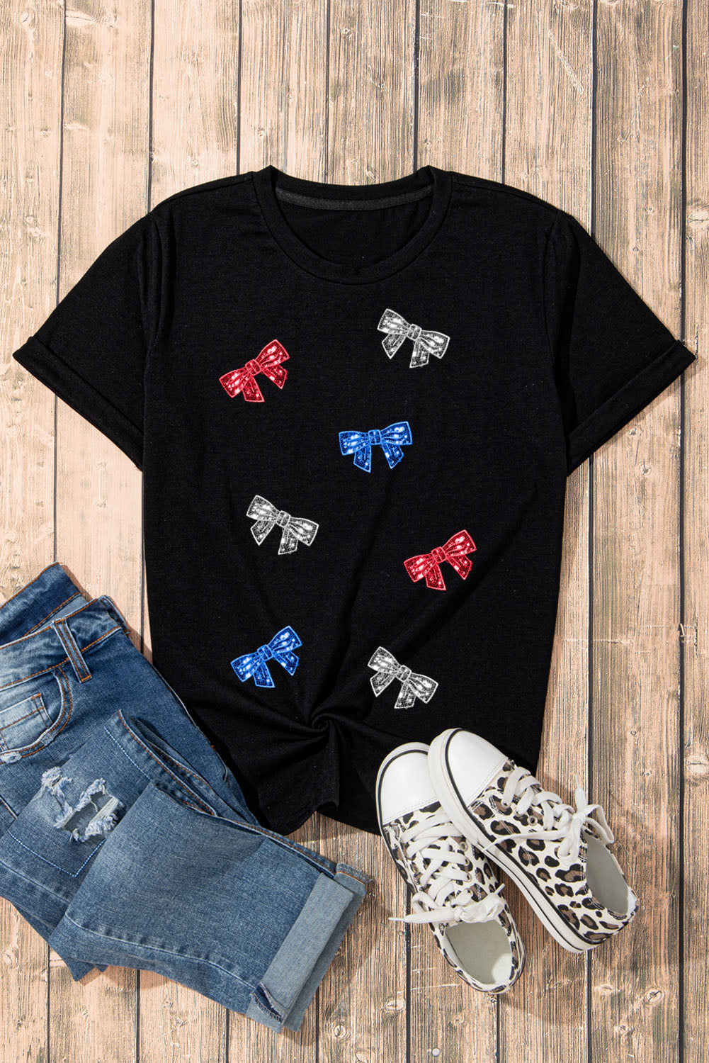 Black crewneck tee with scattered red, blue, and silver bow embellishments.