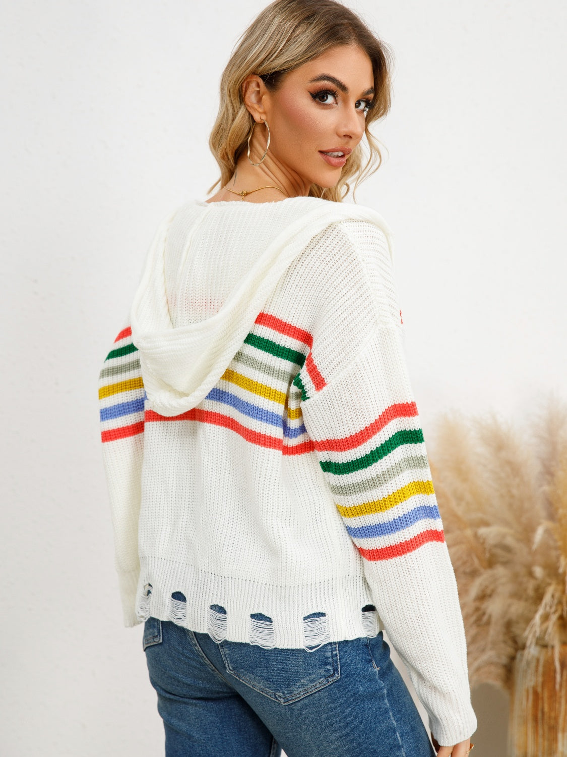 White distressed knit hoodie with rainbow stripes on sleeves and hem.