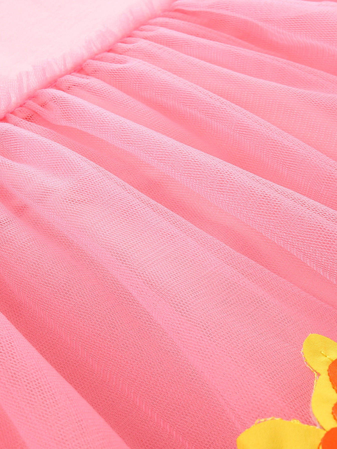 Pink tulle baby dress with a ruffled hem and a partial view of a yellow and orange applique flower.