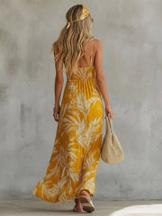 Yellow spaghetti strap maxi dress with tropical leaf print, smocked bodice, and flowing skirt.