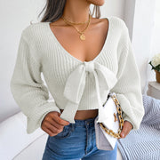 White ribbed knit crop top with V-neck and bow detail, long sleeves.