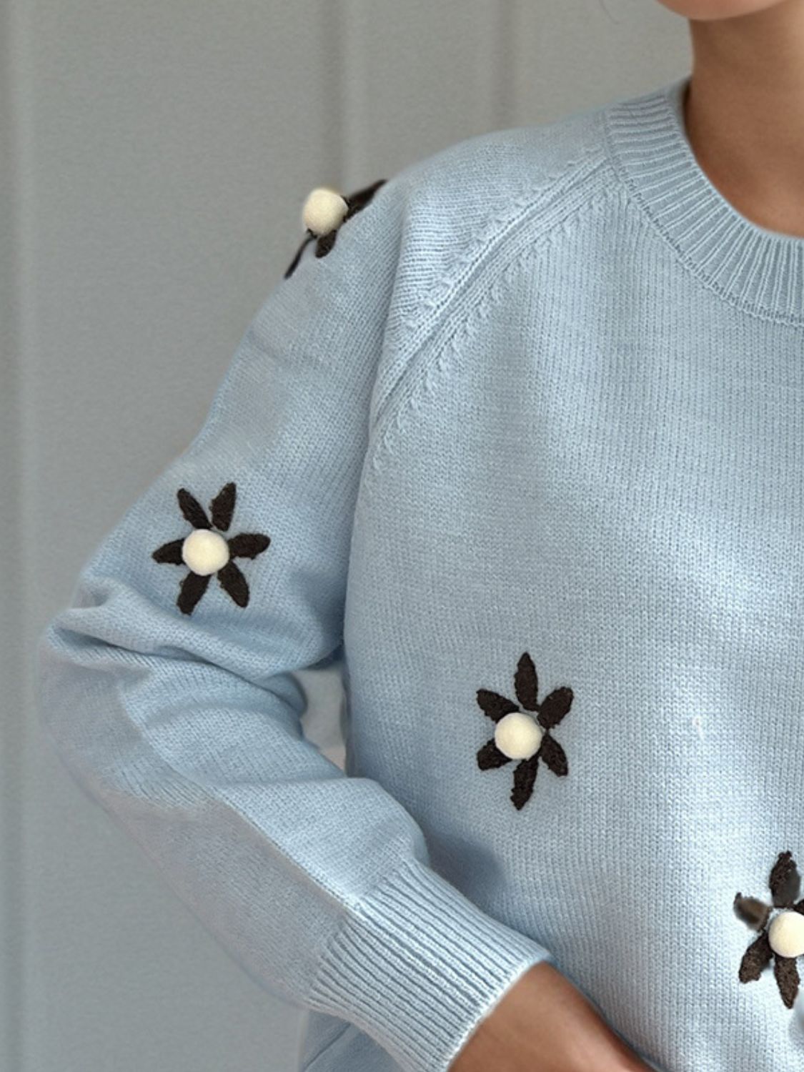 Pastel blue knit sweater with embroidered floral details and pom-pom centers.