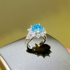 Sterling silver ring with a bright blue oval center stone surrounded by clear accent stones.
