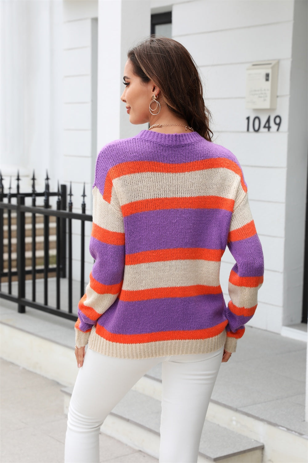 Crewneck knit sweater with bold horizontal stripes in purple, orange, and cream.