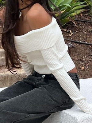 White ribbed knit sweater with fold-over neckline and long sleeves, styled with dark jeans.