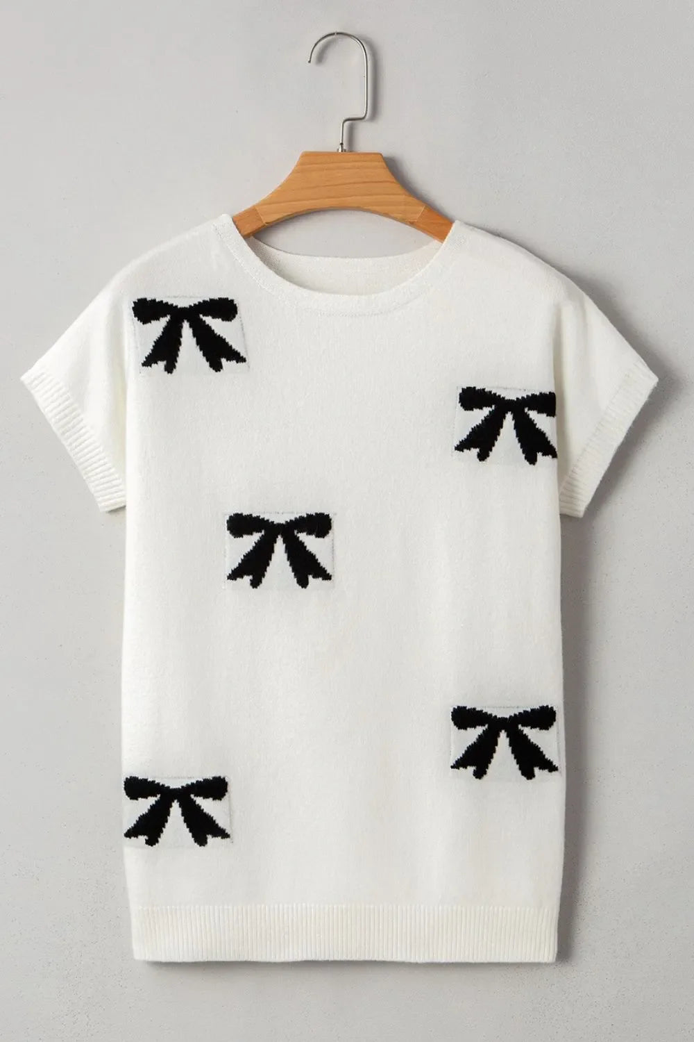 White knit tunic with black bow motif pattern, short sleeves, and crew neck.