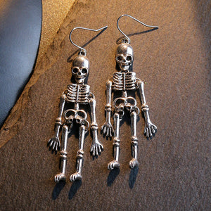 Silver skeleton silhouette drop earrings with articulated limbs.