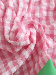 Pink gingham baby dress fabric detail with smocking texture and green accent.