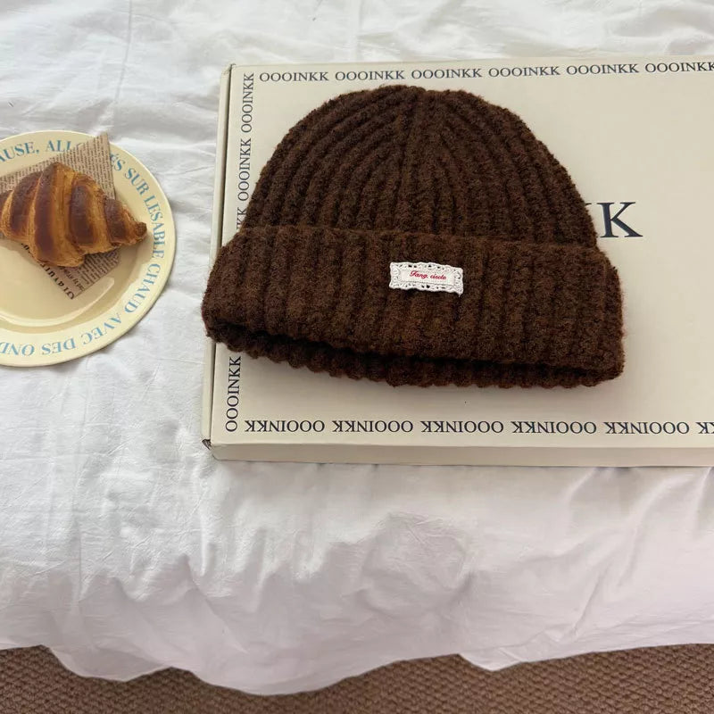 Brown chunky knit beanie with ribbed texture and a white lace detail tag.
