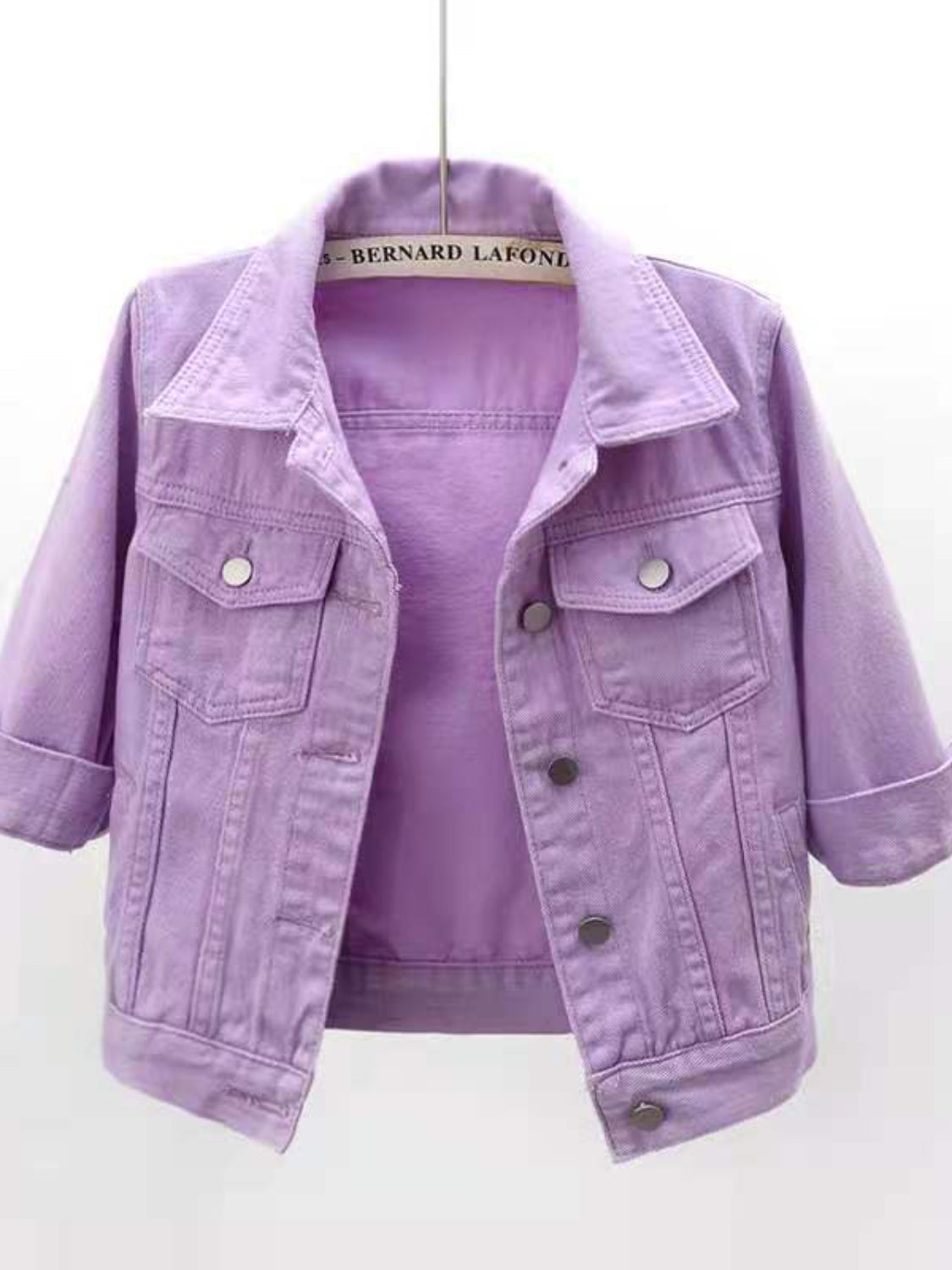 Lavender denim trucker jacket with cropped sleeves and button pockets.
