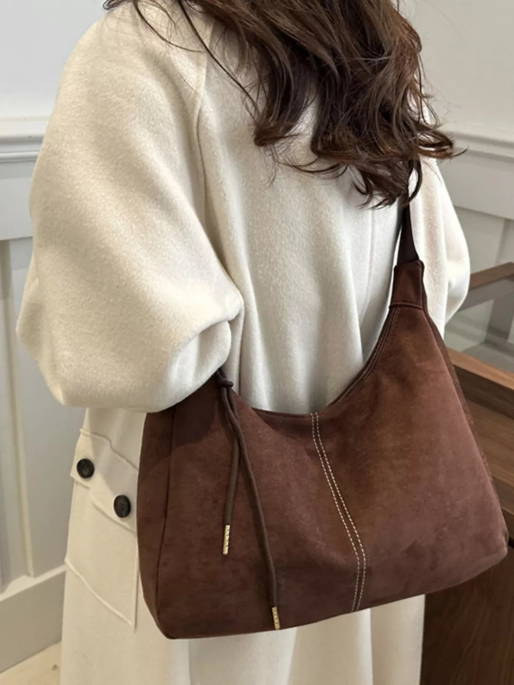 Brown suede crossbody bag with adjustable strap and drawstring detail.