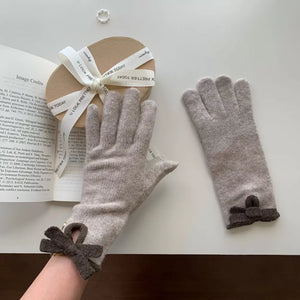 Beige knit gloves with dark gray bows on cuffs.