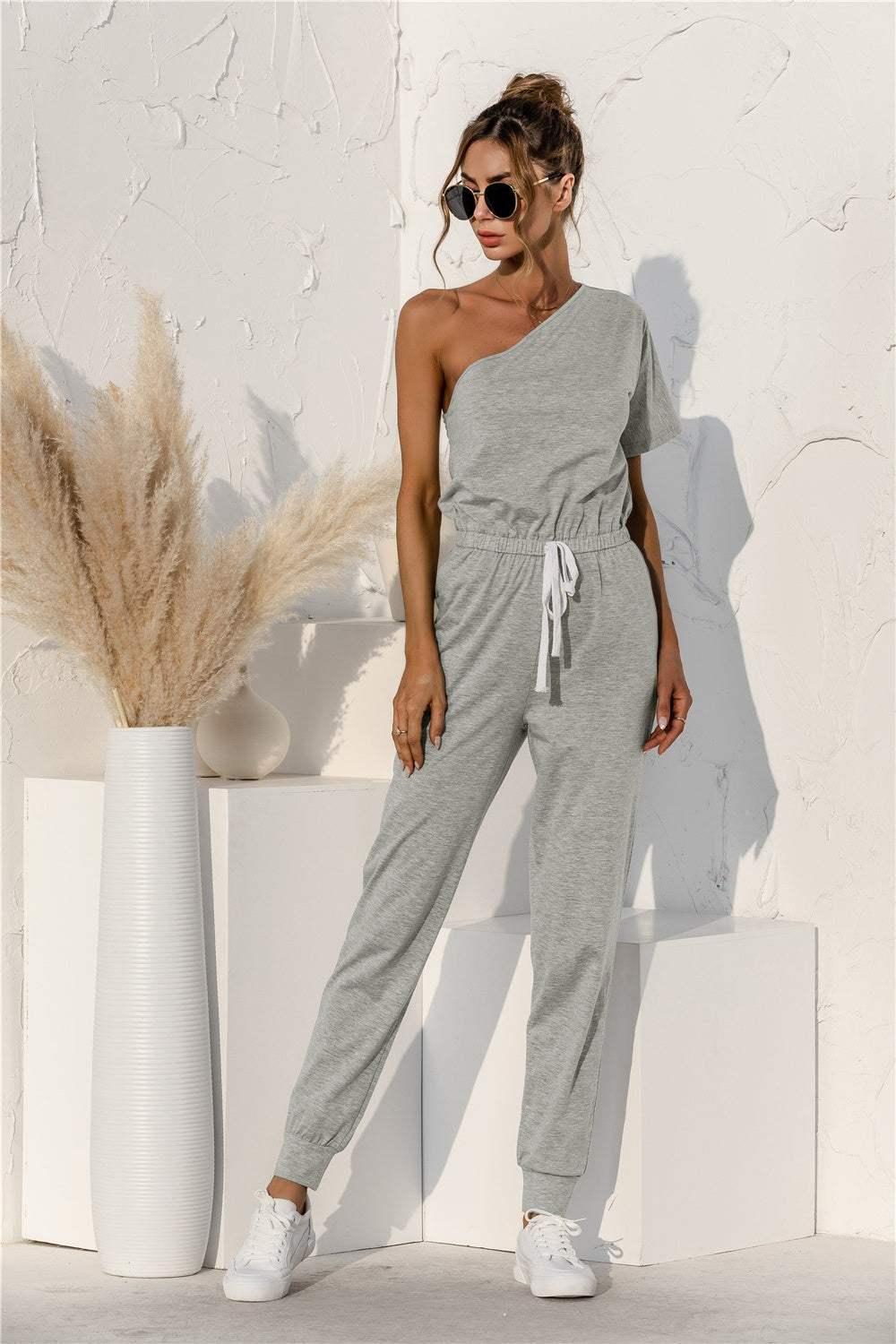 Gray asymmetric sweat jumpsuit with drawstring waist and cuffed jogger legs.
