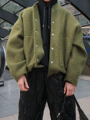 Moss green bouclé cocoon jacket with snap closure and pockets, worn over a black hoodie.