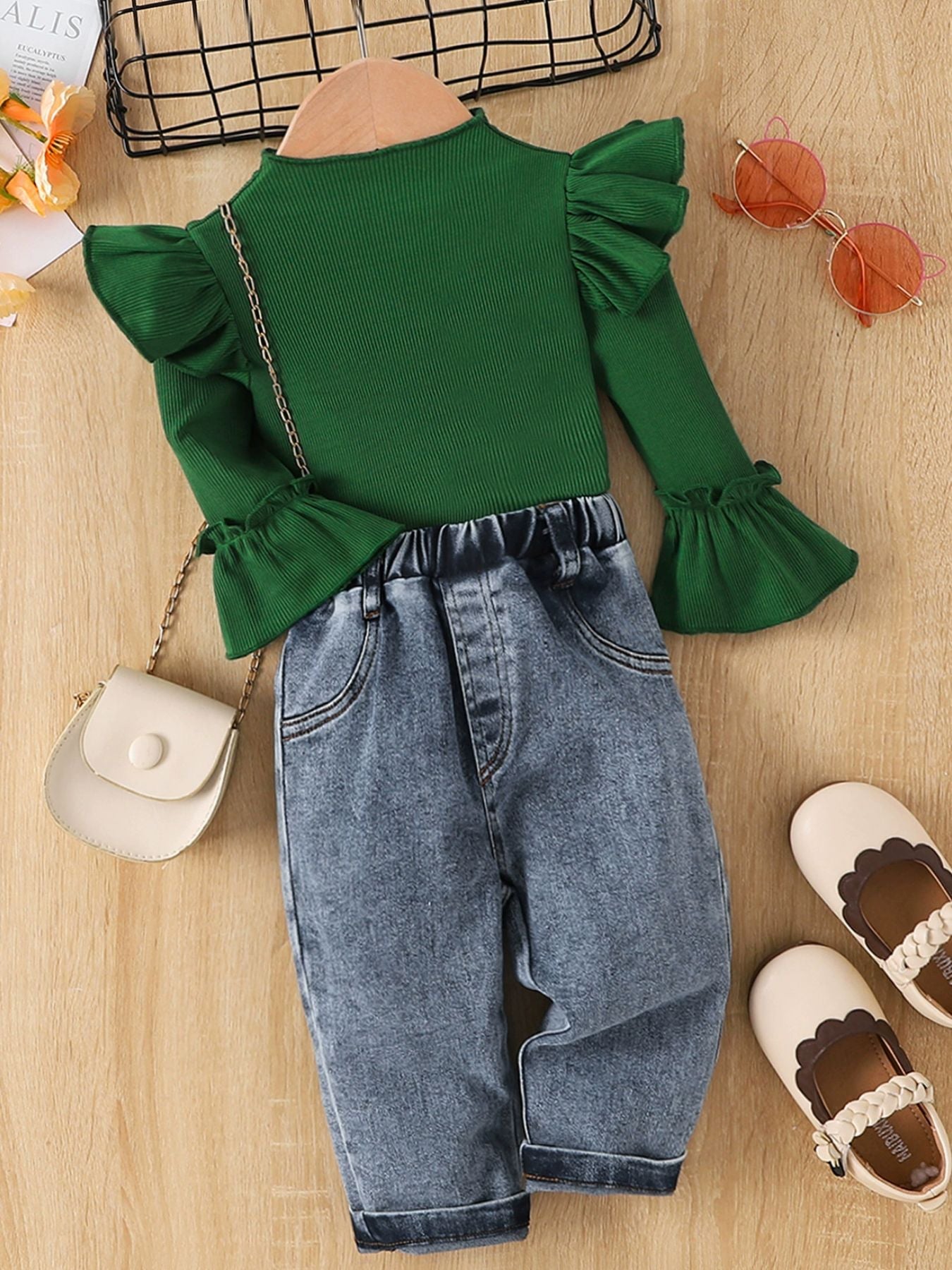 Green ribbed top with ruffle sleeves and bell cuffs paired with denim jeans with elastic waistband.