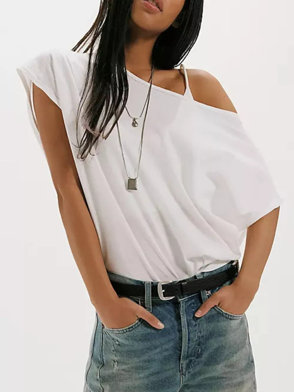 White asymmetrical t-shirt with relaxed fit and one shoulder detail, styled with jeans.