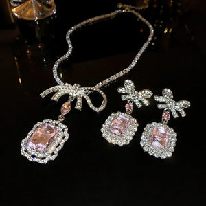 Silver bow pendant necklace and matching crystal earrings with pink gemstones.