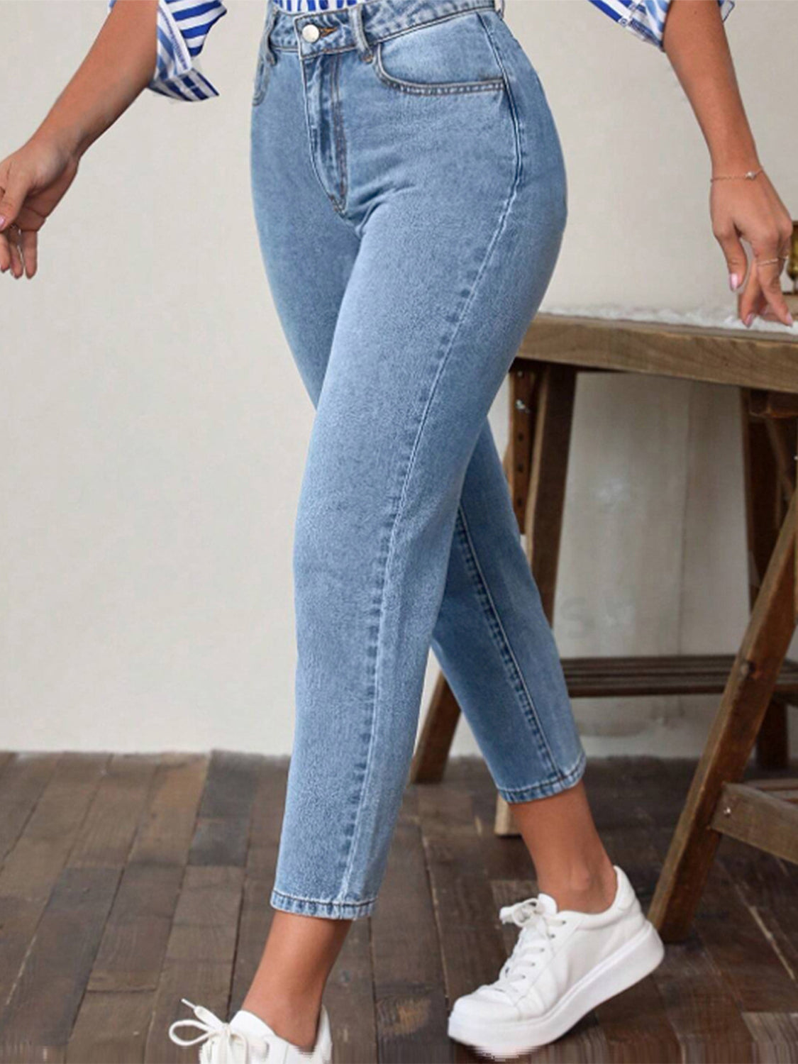 Light wash denim jeans with a slim-fit ankle cut, styled casually with white sneakers.