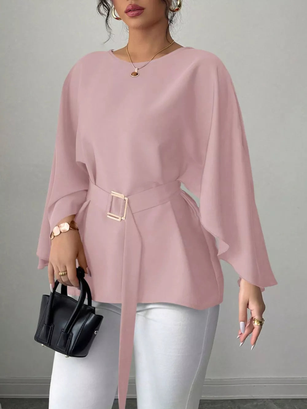 Pink belted blouse with batwing sleeves and gold buckle detail, styled with white pants.