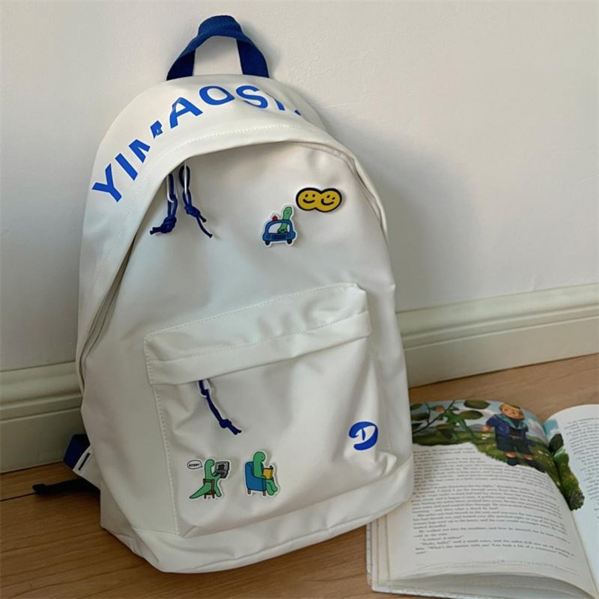 Off-white nylon backpack with blue drawstring details and fun cartoon patches.