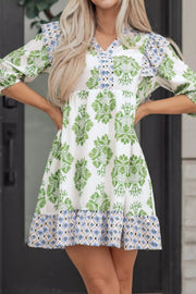 Mini dress with green floral print, ruffled neckline, and geometric hem.