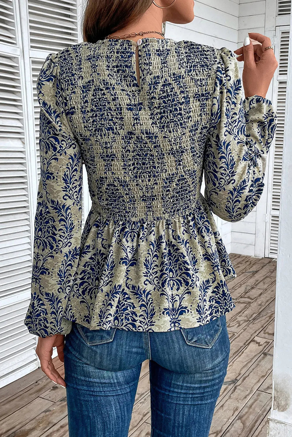 Navy damask print smocked peplum blouse with long sleeves and a keyhole back.