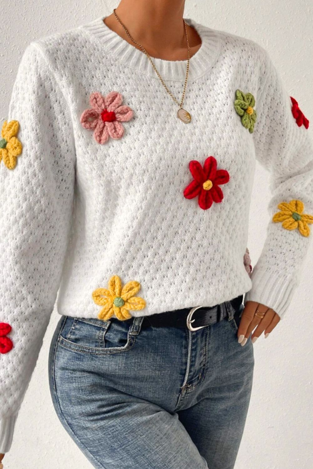 White knit sweater with colorful crochet floral embellishments and a textured pattern.