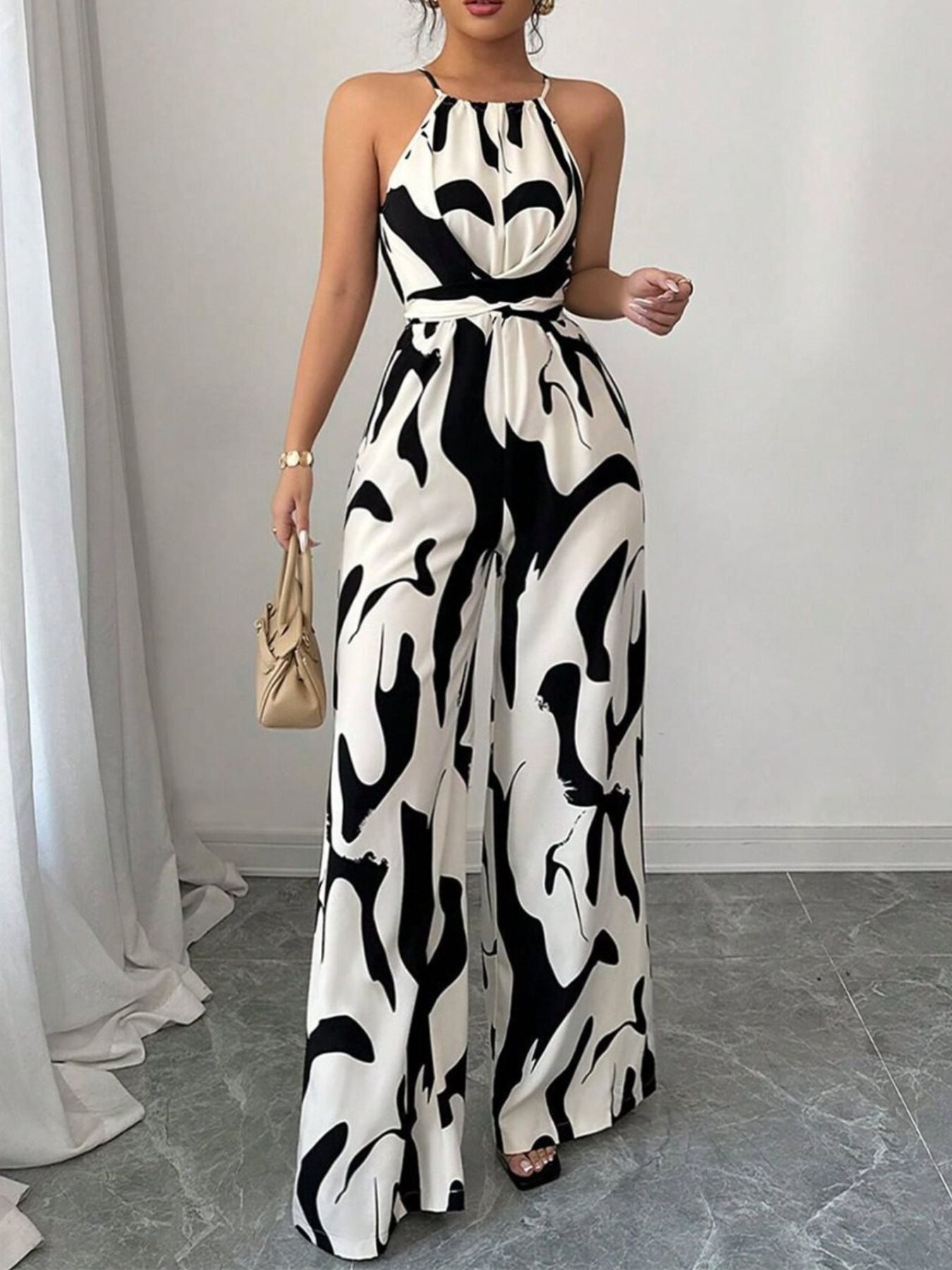 Chic abstract print halter jumpsuit in black and white, featuring wide legs and a tie waist.