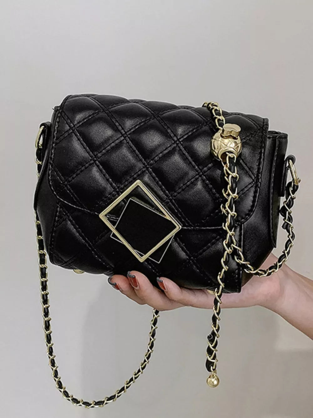 Black quilted crossbody bag with gold chain strap and geometric charm detail