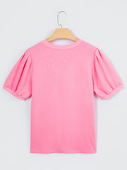 Pink cotton blouse with short puff sleeves and a round neckline.