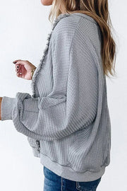 Gray waffle knit top with fringe trim and cuffed sleeves.
