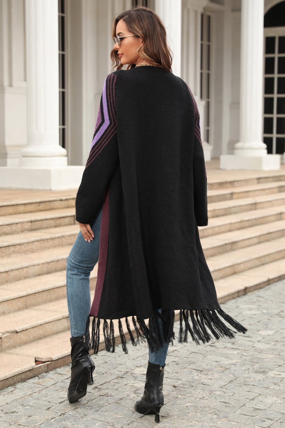 Black cardigan with geometric trim on sleeves and fringed hemline, styled with jeans.