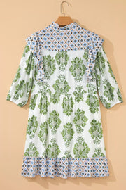 White mini dress with green floral print, ruffled neckline, and patterned hem.