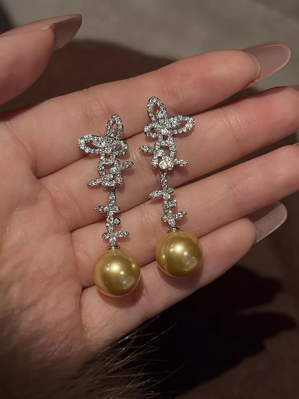 Lustrous butterfly pearl drop earrings with diamond accents in gold tone.