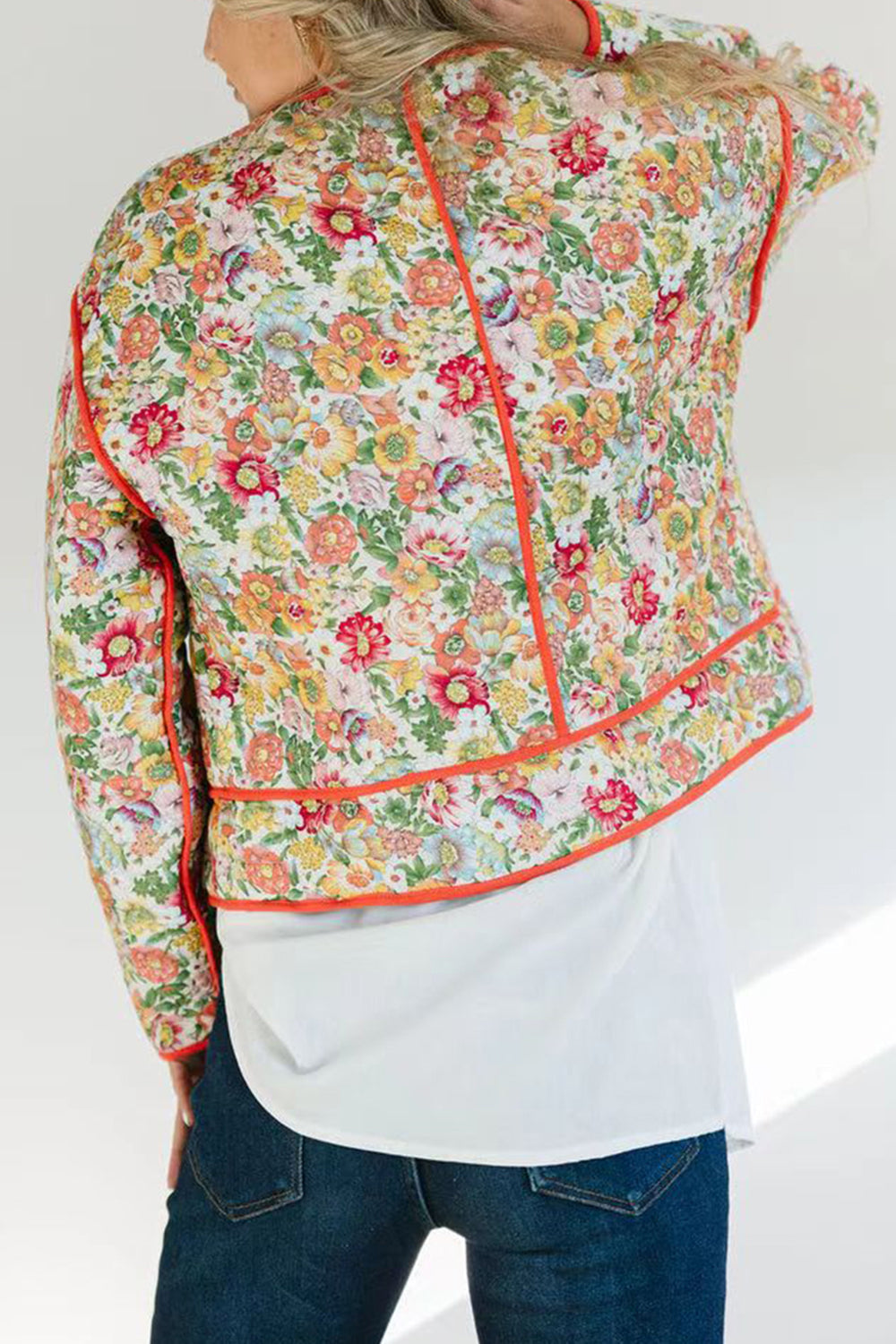 Floral quilted jacket with contrast piping in orange-red, featuring a white base and colorful floral print.