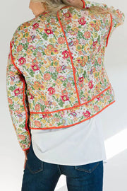 Floral quilted jacket with contrast piping in orange-red, featuring a white base and colorful floral print.