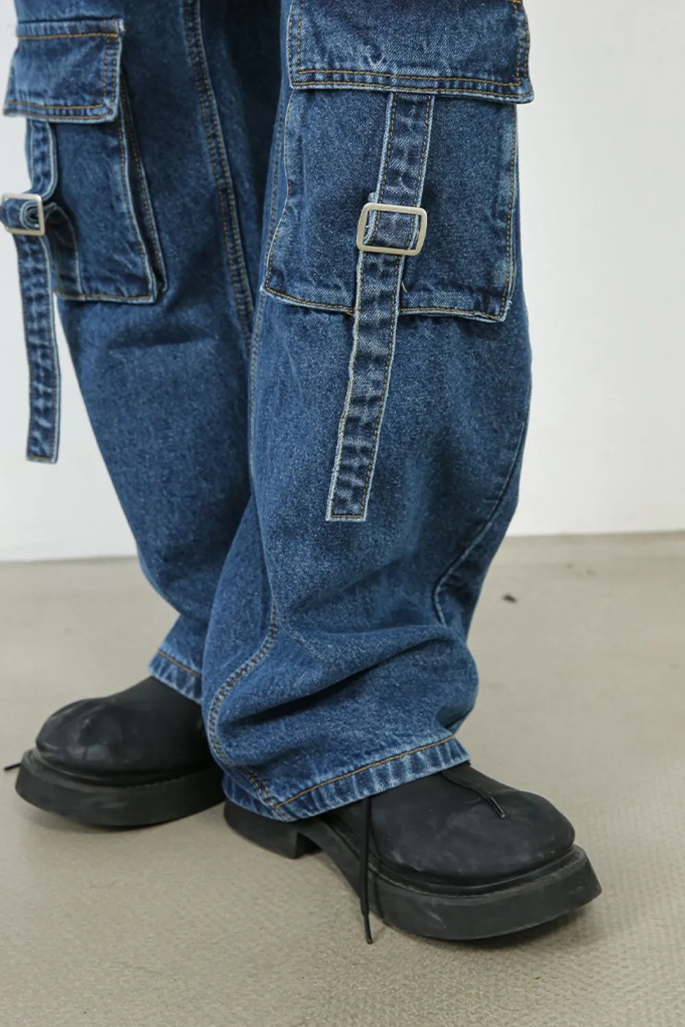 Medium wash denim cargo pants with buckle strap pockets and wide legs.