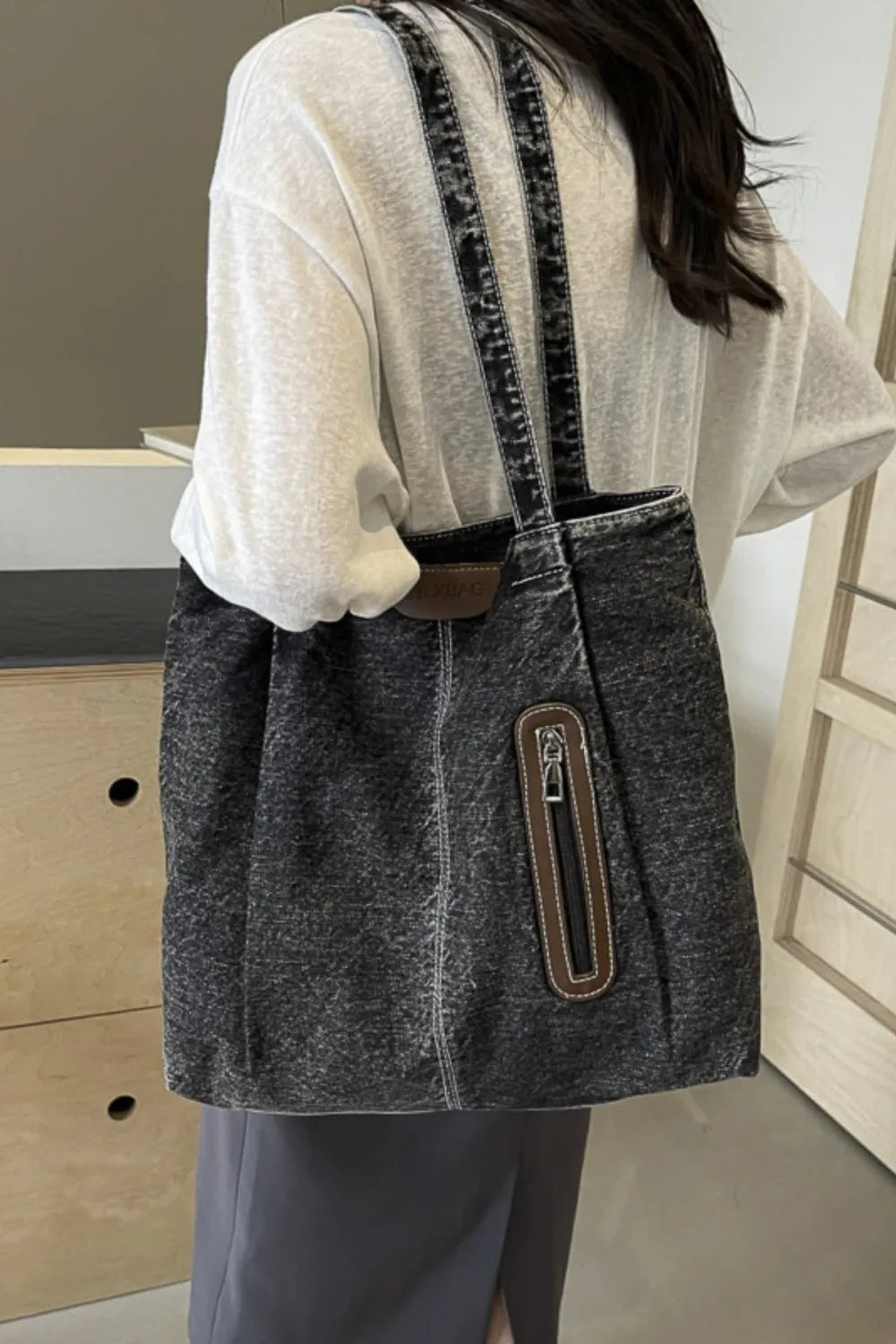 Denim tote bag in dark wash with leather trim and front zipper pocket.