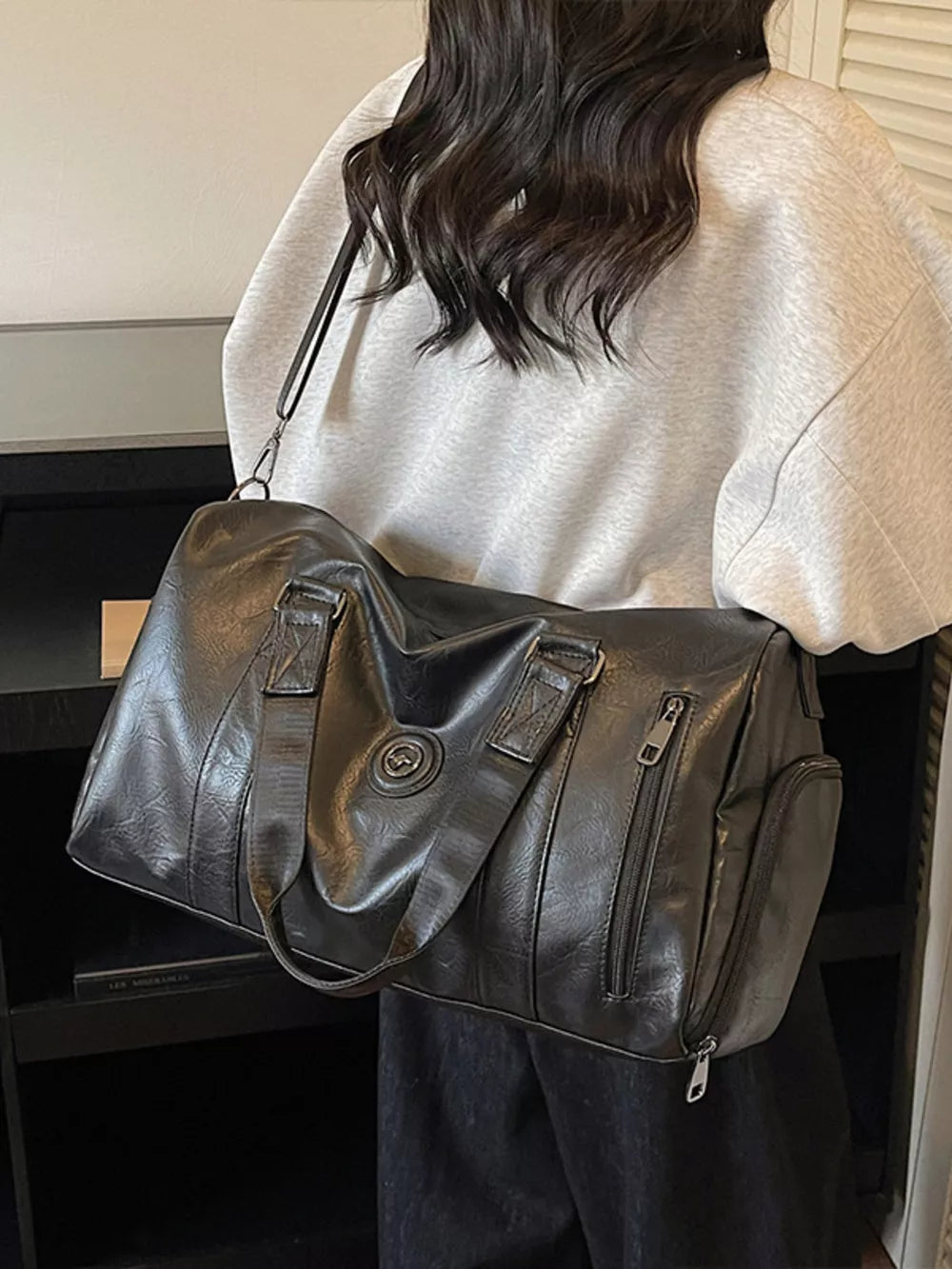 Black pu leather duffel bag with zippered pockets and top handles.