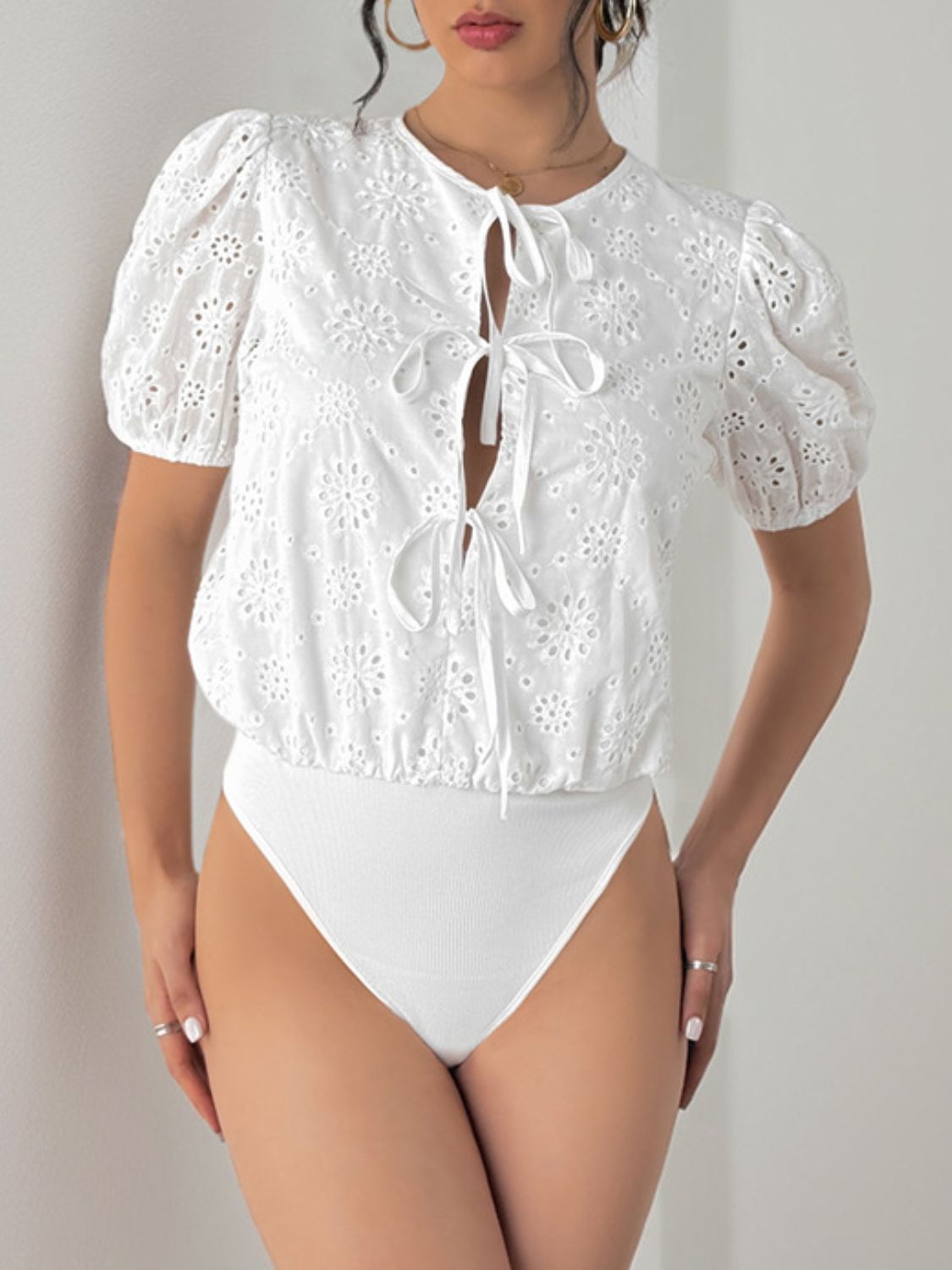 White eyelet bodysuit with puff sleeves and tie front detail.